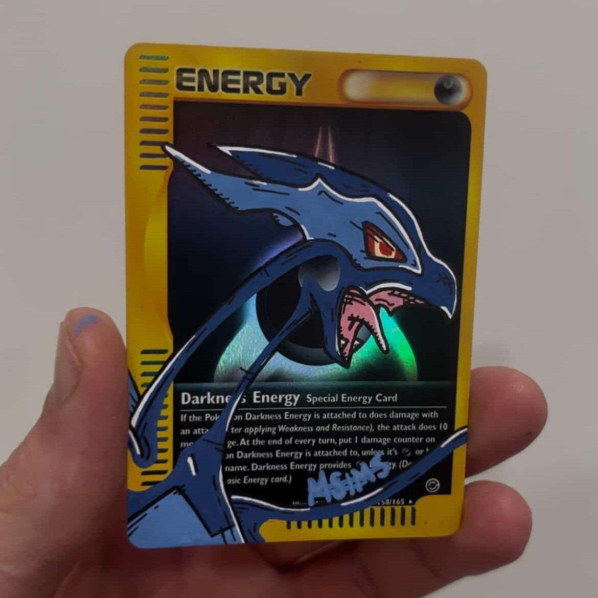 Hand holding a trading card with a dragon design on a yellow border